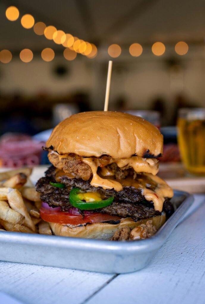 Close-up of a gourmet cheeseburger with fries, tomato, green pepper, and sauce, served on a tray in a restaurant.