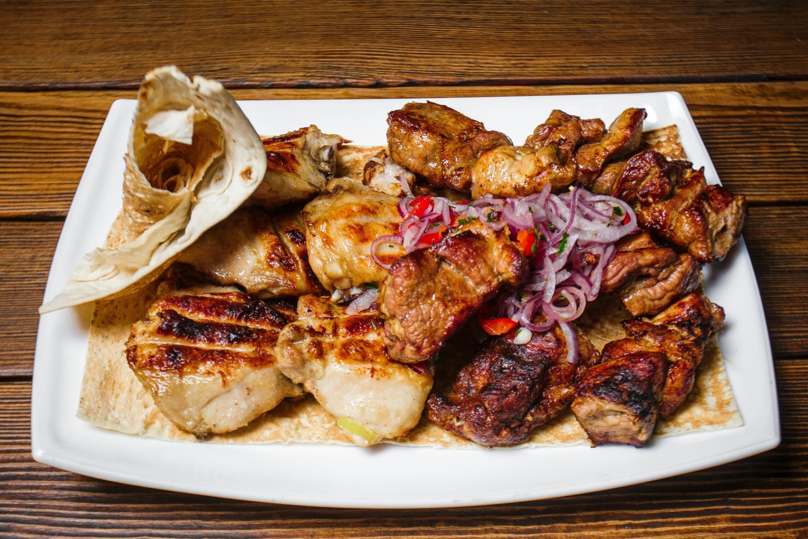 Exquisite grilled meat selection served with onions and flatbread on a wooden table.